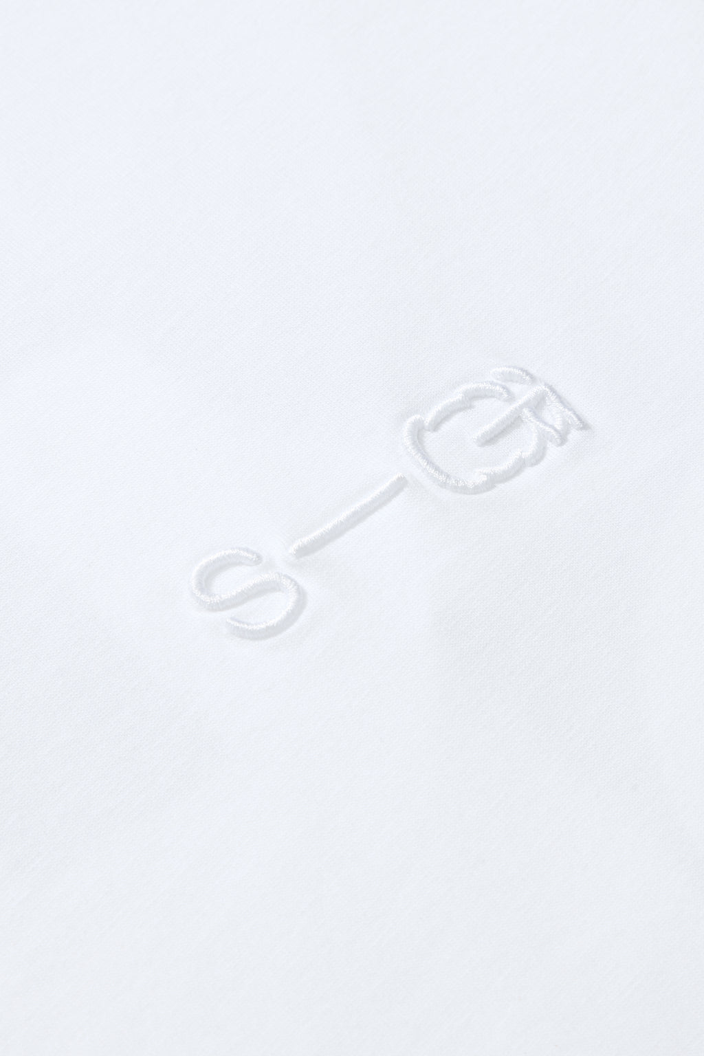 Close-up of raised S-G embroidery on white cotton T-shirt, showing detail and texture.
