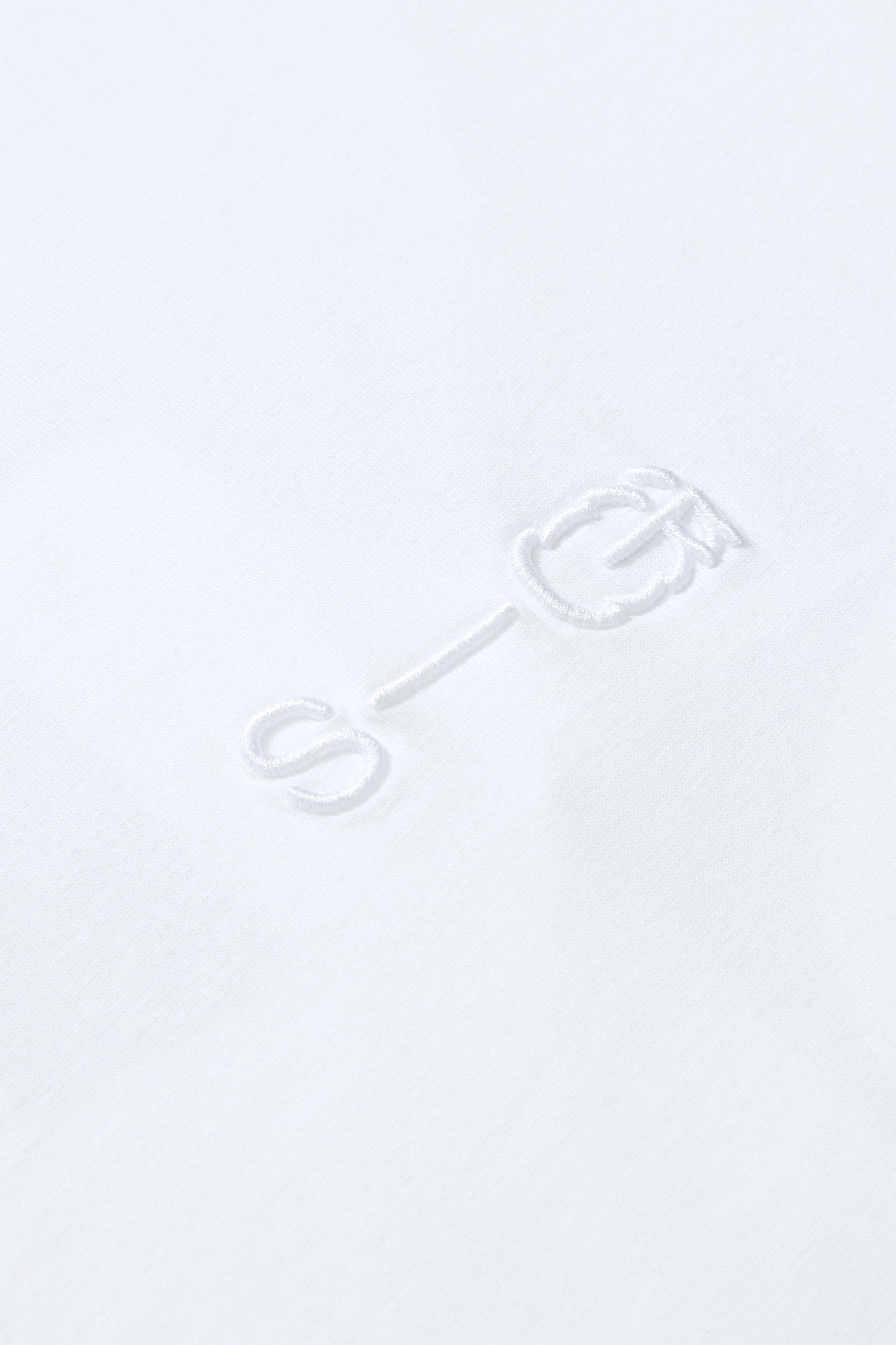 Close-up of raised S-G embroidery on white cotton T-shirt, showing detail and texture.