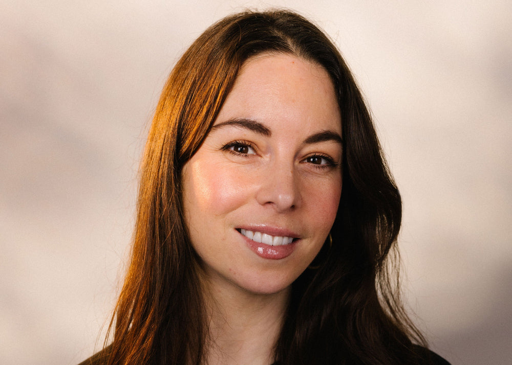 Woman with long dark hair smiling against a plain background