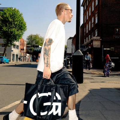 Man walking on a city street with a large black bag featuring white text.