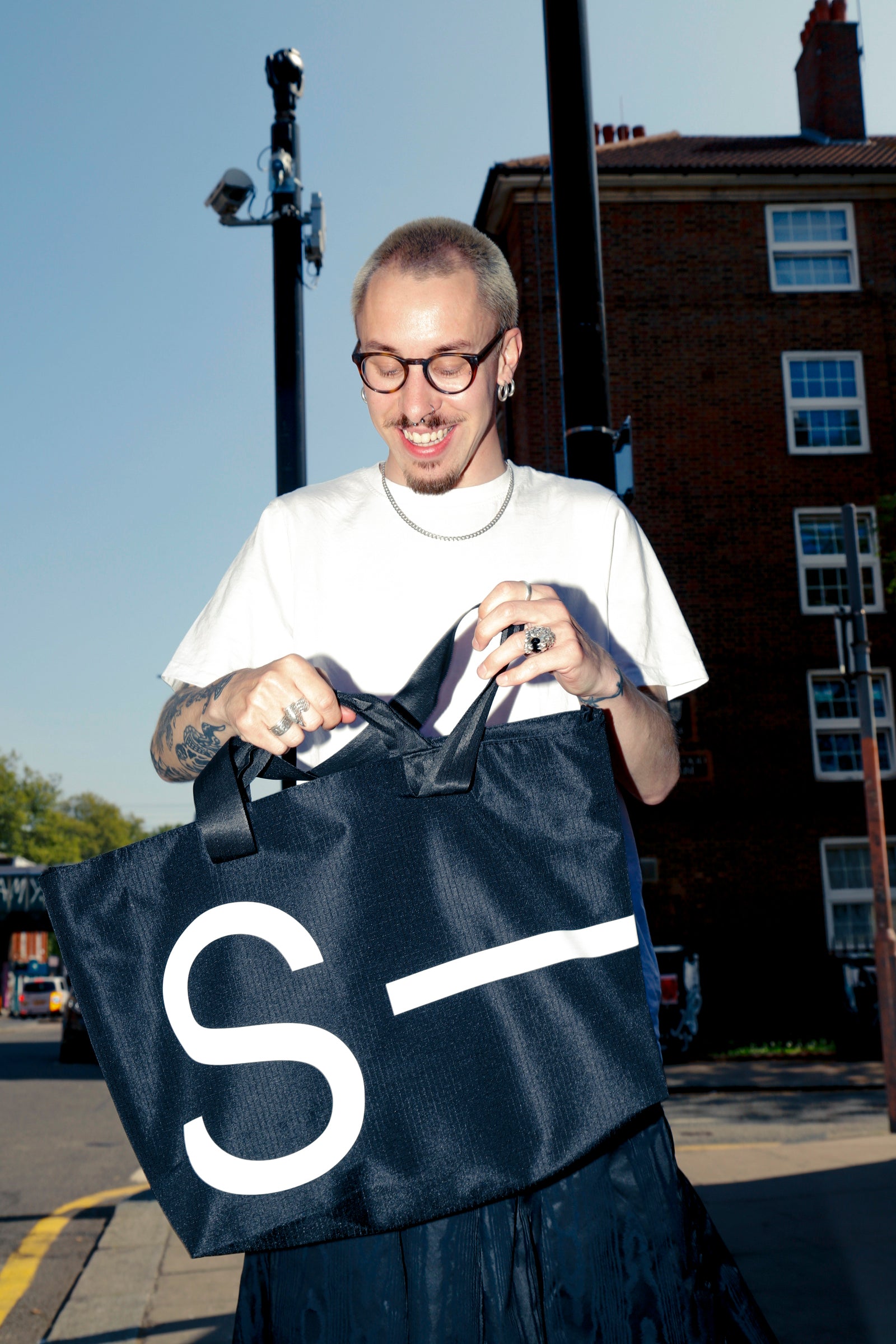 Person holding a black bag with a white 'S' logo on a street.