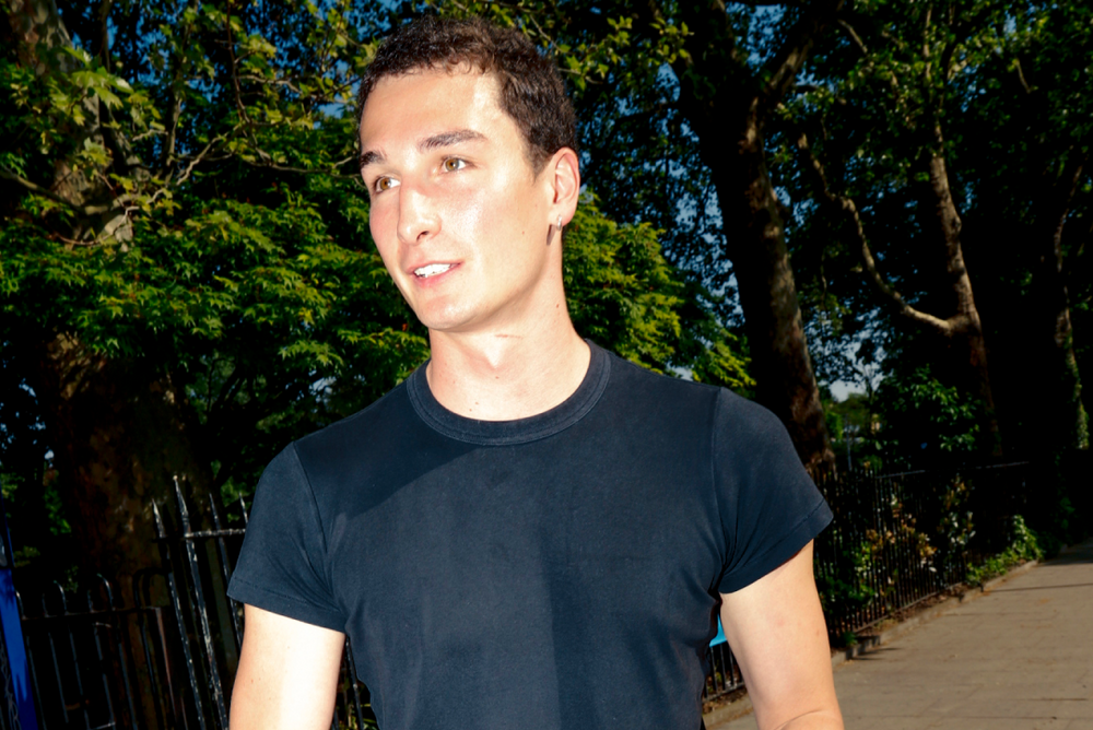Man holding a black bag with a logo, standing outdoors on a sidewalk.