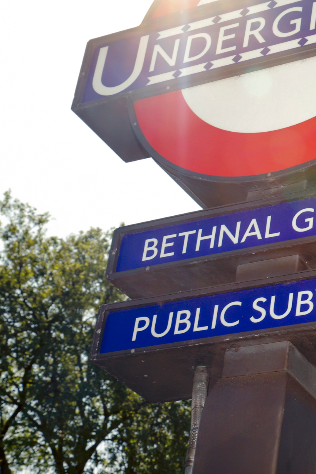 Underground sign with 'Bethnal Green' station name against a blurred tree background