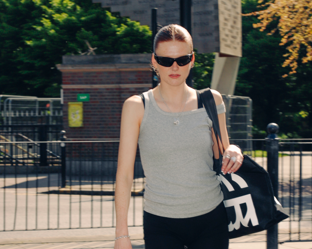 Woman crossing the street with a green pedestrian signal, wearing sunglasses and carrying a black bag.