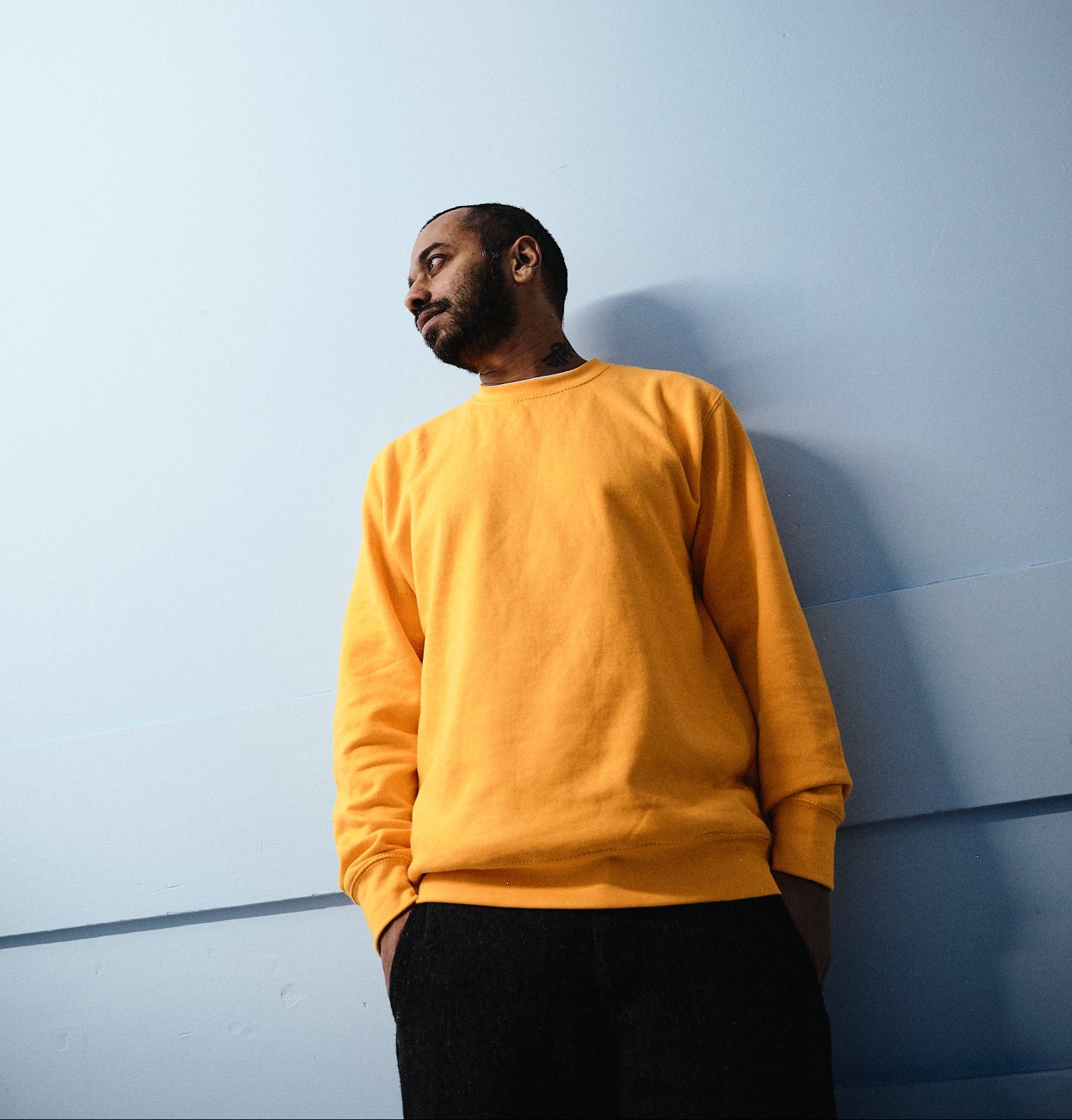 Man wearing a yellow sweatshirt against a light blue wall